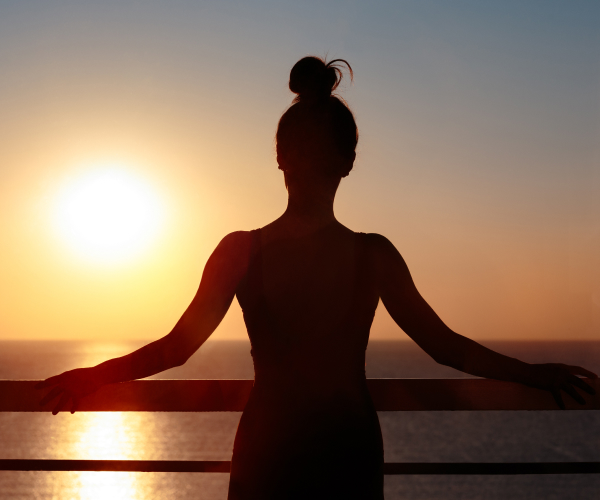 Photo of a woman looking at the water from a cruise ship, backlit by the sun